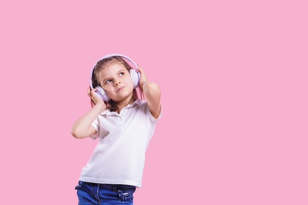 Girl listening to music in headphones on pink . Cute child enjoying happy dance music, close eye's and smile posing   