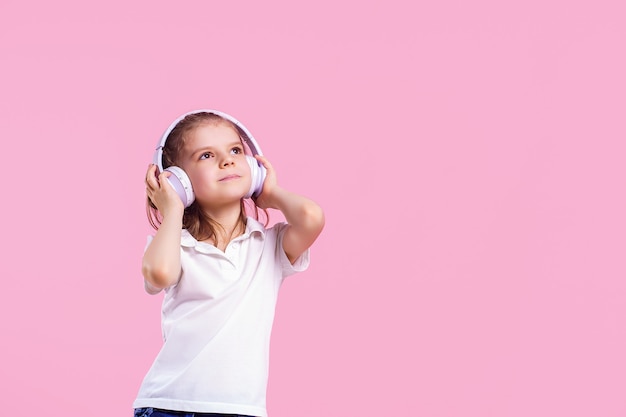 Girl listening to music in headphones on pink wall.