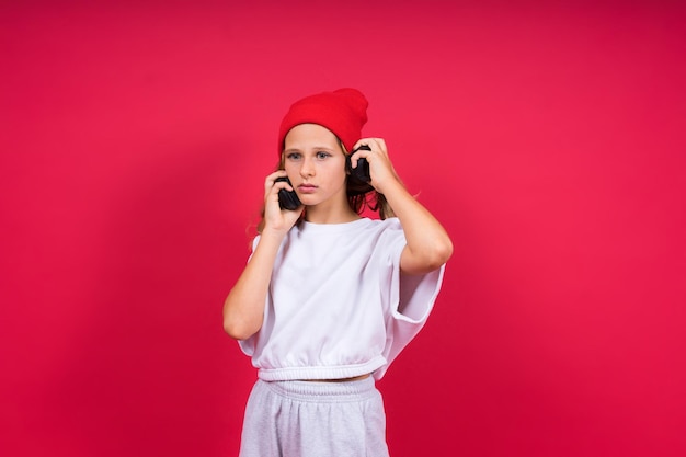 Girl listening to music in headphones on red background Cute child enjoying dance music smile