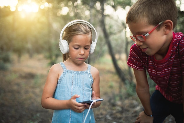 girl listening music while using mobile phone by brother in forest