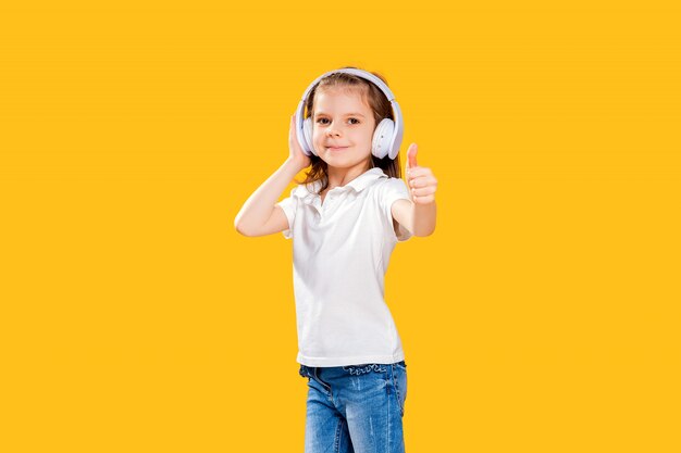 Ragazza che ascolta la musica in cuffie senza fili su giallo. ragazza danzante. piccola ragazza felice che balla alla musica. bambino sveglio che gode della musica da ballo felice.