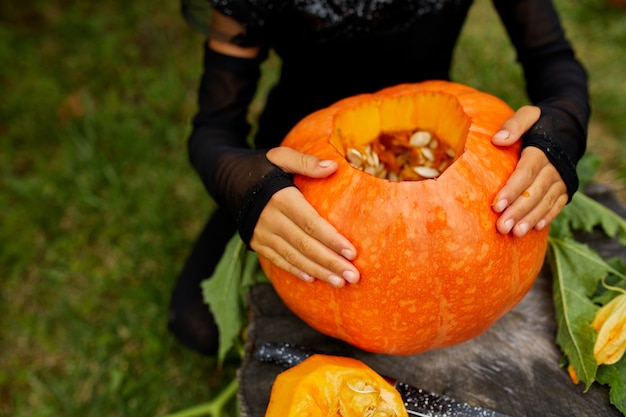 女の子、小さな子供の手はハロウィーンのために彫る前にカボチャを持って、ジャック・オー・ランタンを準備します。パーティーの装飾、小さな家族のヘルパー、上面図、クローズアップ、上からの眺め、コピースペース