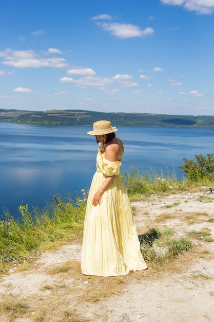 A girl in a long dress standing on a cliff by the bay