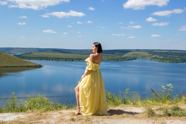 A girl in a long dress standing on a cliff by the bay