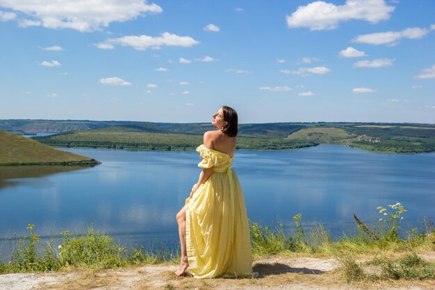 A girl in a long dress standing on a cliff by the bay