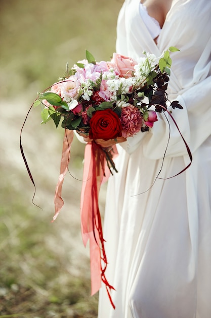 Girl in a long dress stands in a field with wreath on her head and bouquet of flowers in her hands