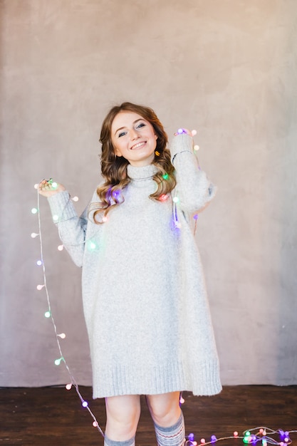 Girl in a long light sweater, jacket, and garland with Christmas lights