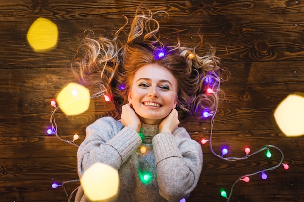 Foto ragazza con un maglione lungo e leggero, una giacca e una ghirlanda con luci natalizie