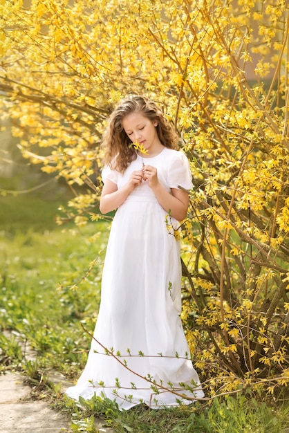 Foto una ragazza in un lungo abito bianco in un giardino fiorito forsizia gialla