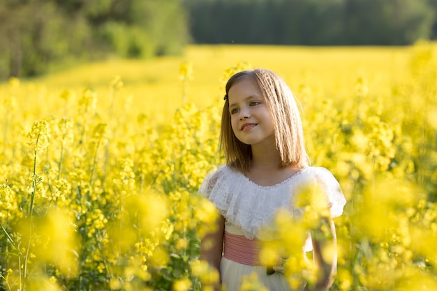 girl in a long white dress in a rapeseed field in summer