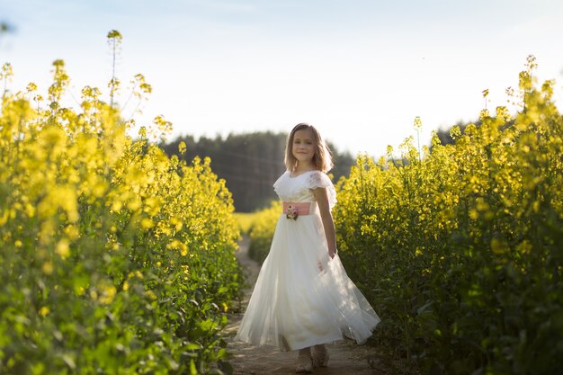 girl in a long white dress in a rapeseed field in summer