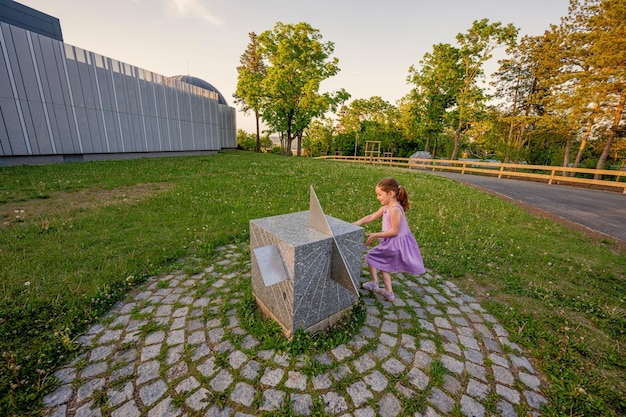 Girl look at sun watches stone cube in planetarium outdoor