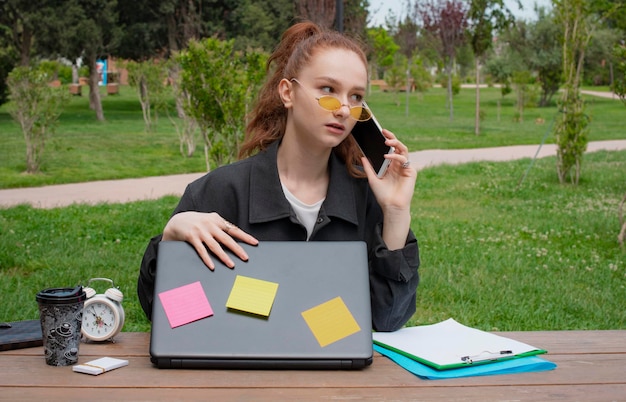 Girl looking aside closing laptop talking on phone in park