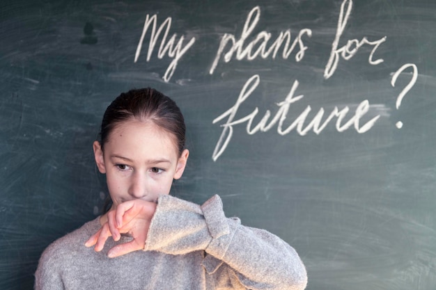 girl looking away while standing by blackboard with text in classroom