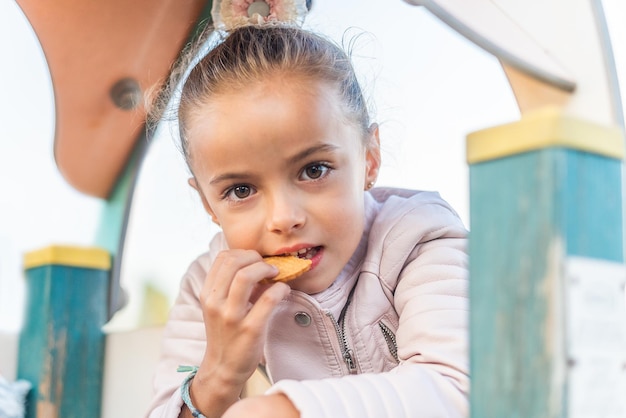 Girl looking at camera eating a cookie in a playground