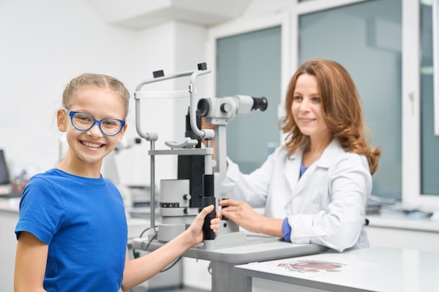 Ragazza che guarda l'obbiettivo mentre l'oculista controlla la vista