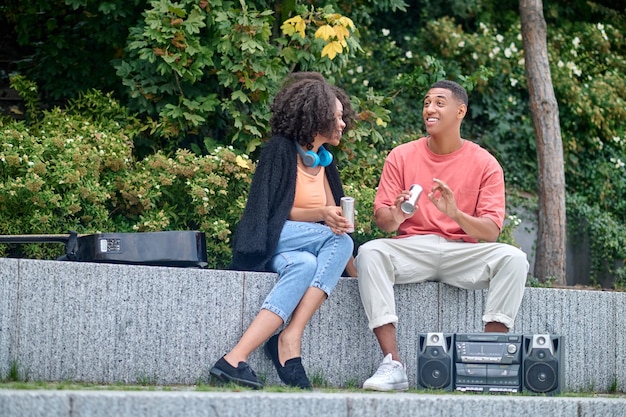 Girl looking at cheerful guy sitting talking in park