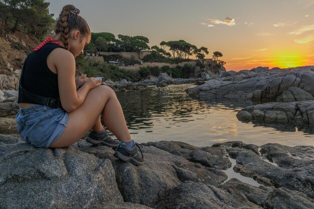 스페인 카탈로니아의 해변에서 일출 동안 휴대폰을 바라보는 소녀