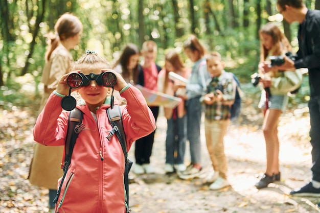 Photo girl looking into binoculars kids in green forest at summer daytime together