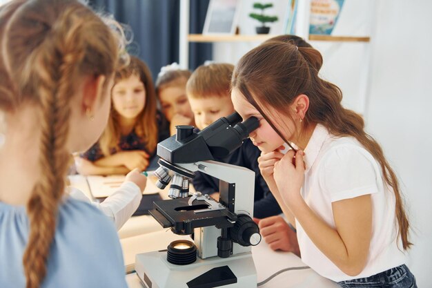 Girl looking into microscope Group of children students in class at school with teacher