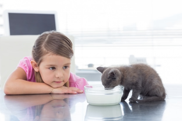 ボウルから牛乳を飲む子猫を見ている少女