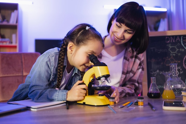 Girl looking at onion cells in microscope while her mother sitting near