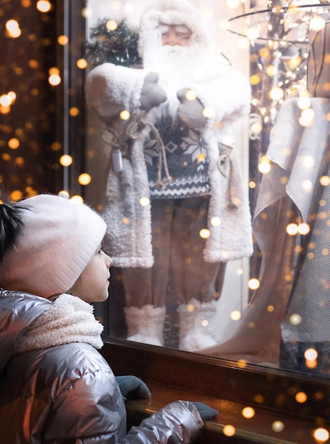 Foto ragazza che guarda dalla finestra alle decorazioni natalizie in un negozio