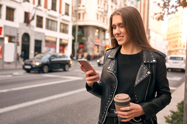 Photo girl looking at phone and holding a coffee