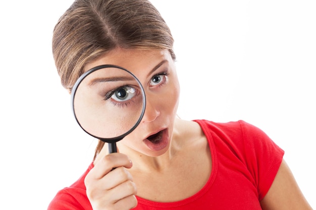 Girl looking through a magnifying glass and looking surprised isolated on white