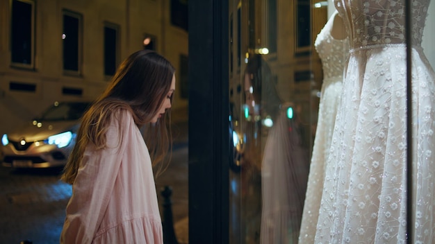 Girl looking wedding store showcase standing on night street closeup white gown