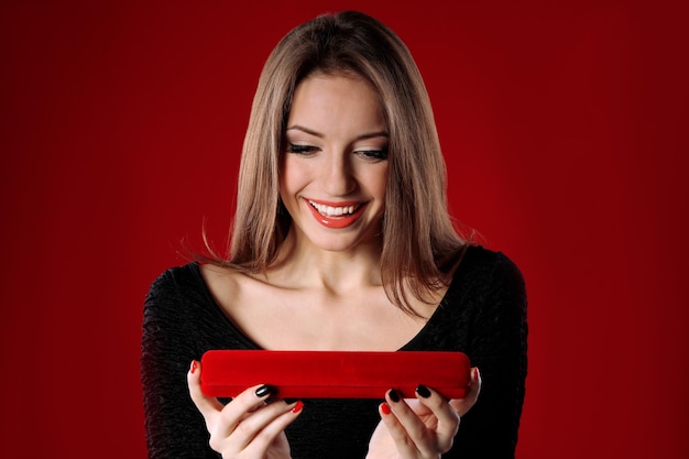 Girl looks at box with jewelry gift on color background