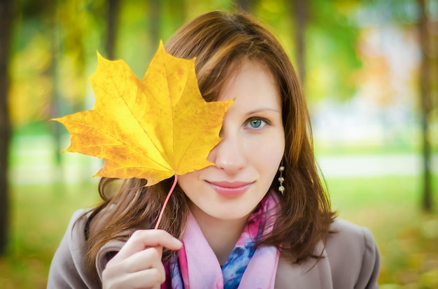 The girl looks through the yellow autumn leaf