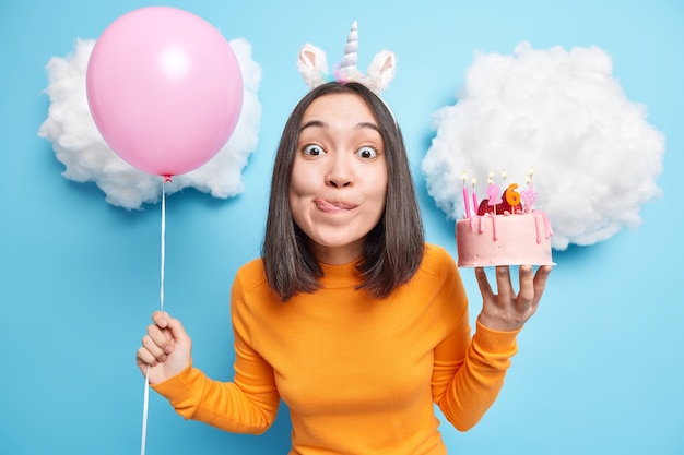 Girl looks with temptation at camera licks lips wants to eat
delicious cake has special occasion celebrates 26th bday holds
inflated balloon