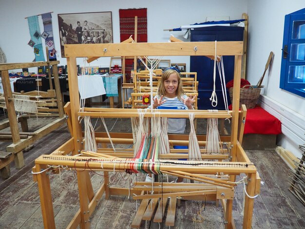 소녀 베틀과 실 카펫 의류 및 직조 가정용품 생산을 위한 골동품 장비 실과 실은 칸막이 위로 뻗어 있습니다. Trsic Loznica 세르비아 민족 관광