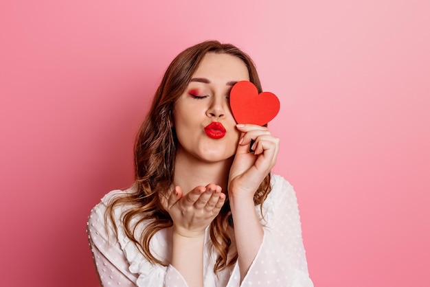 Girl in love sends air kiss on valentine's day isolated on pink background