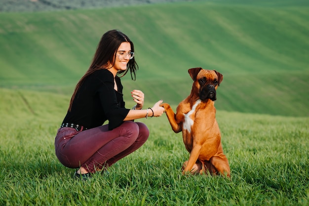 緑の牧草地で彼女のボクサー犬を愛する少女