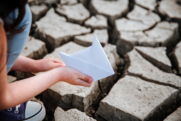 Foto la ragazza abbassa la barchetta di carta sulla terra secca e crepata riscaldamento globale