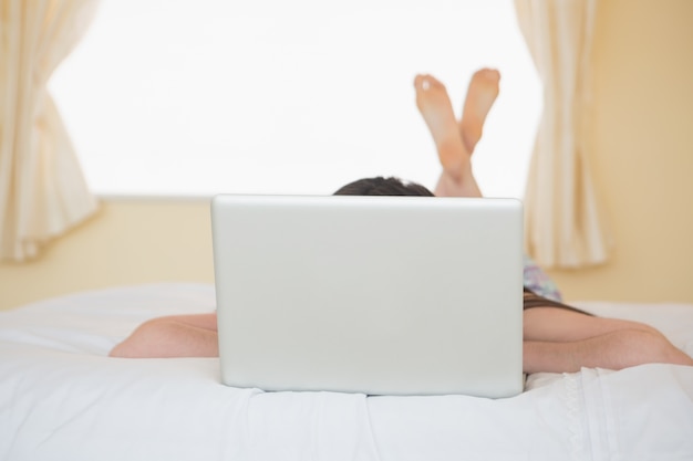 Girl lying on a bed hiding behind a laptop