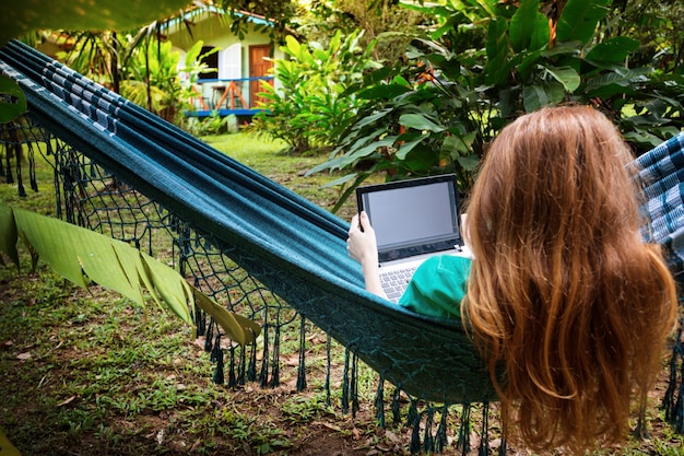 girl lying in a hammock and working on a laptop at the garden