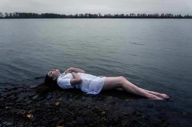 Girl lying on the rock of dark river . Ophelia conceptual