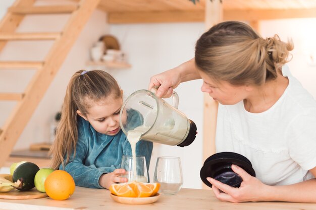 女の子は母親とブレンダーでスムージーを作ります