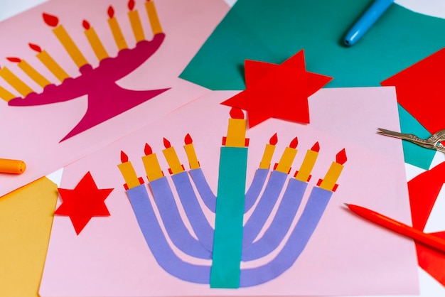 A girl makes a card for happy hanukkah with her hands a\
candelabra and candles on the card