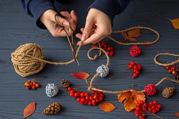 The girl makes a garland of autumn leaves berries and cones
view from above autumn mood autumn background