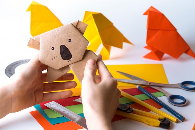Девушка делает оригами коалу из цветной бумаги бумага линейка карандаши нож интересное хобби