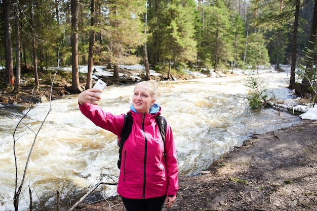 Girl makes a selfie against the background of a mountain stream and forest