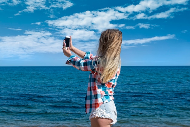 The girl makes a selfie on the phone against the background of the sea.