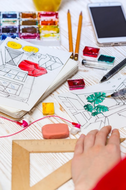 Girl  makes a sketch of the interior. the hand of the girl artist and  sketch, markers, pencil, eraser, ruler, paints, calculator on a wooden background