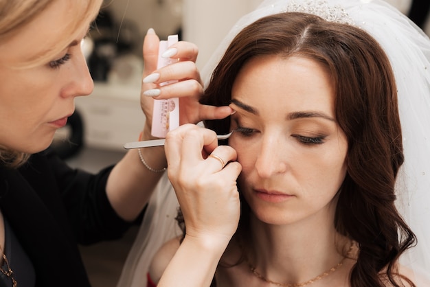 The girl makeup artist glues the eyelash bundles on the eye of the girl model.