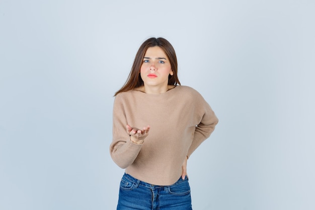 girl making asking question gesture in sweater, jeans and looking serious 