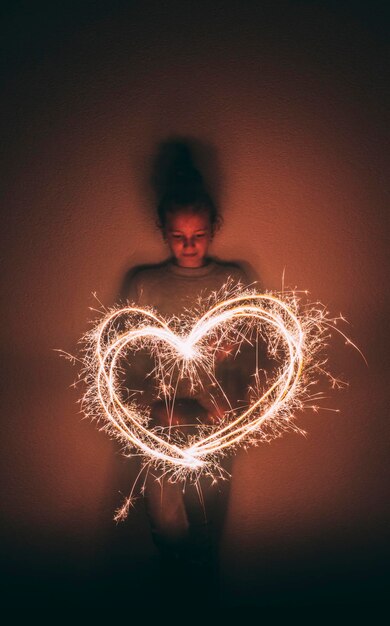 Foto ragazza che fa la forma di un cuore con uno scintillante nella camera oscura contro il muro